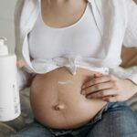 Close-up of a pregnant woman applying moisturizing lotion to her belly for skincare and maternity care.