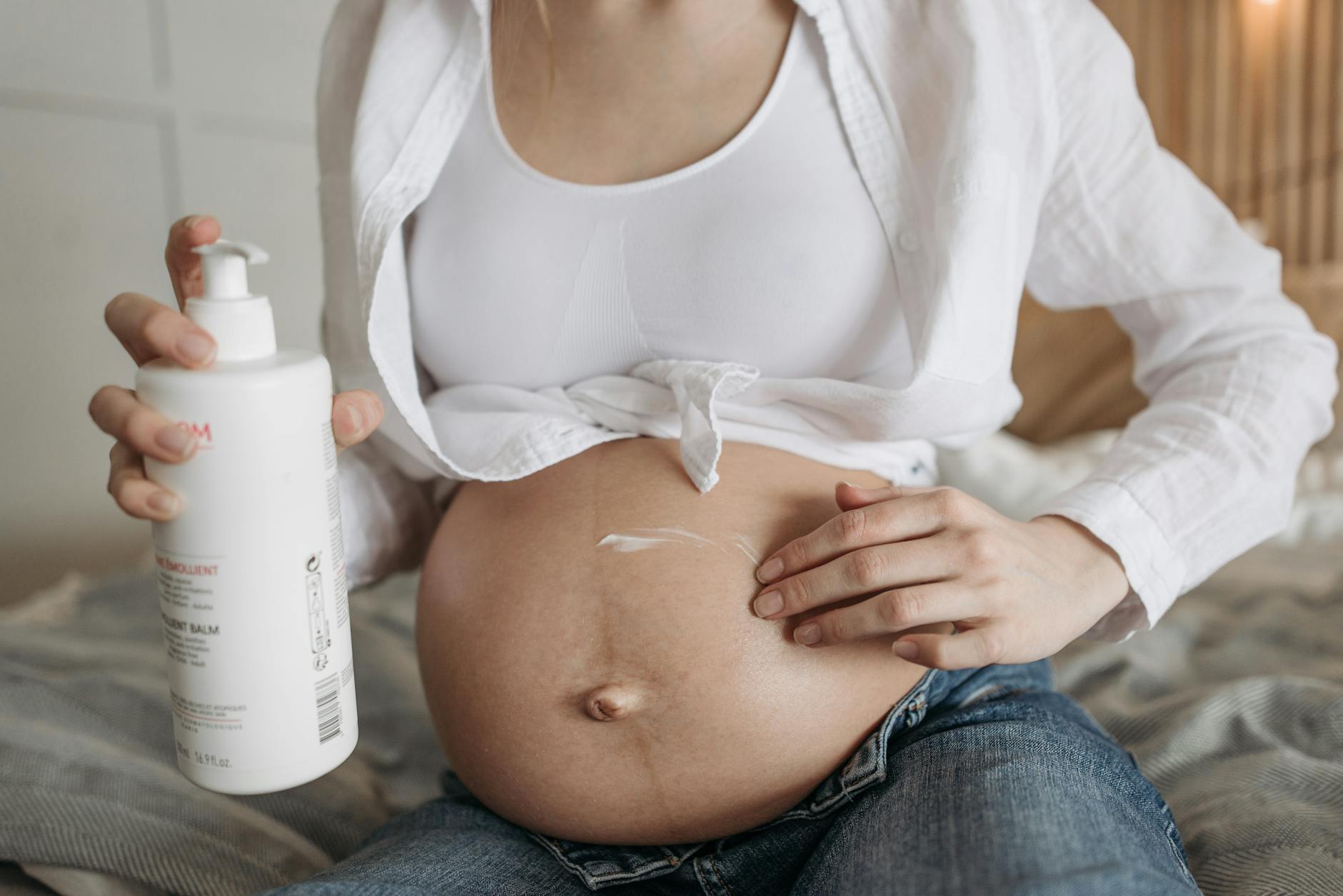 Close-up of a pregnant woman applying moisturizing lotion to her belly for skincare and maternity care.