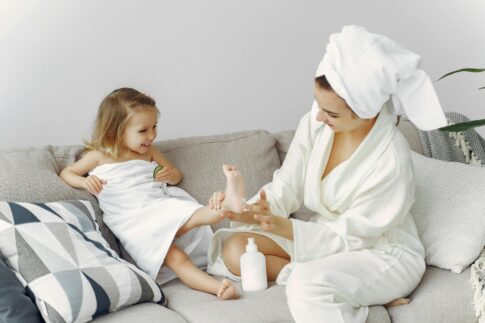 A mother and daughter enjoy bonding time on the sofa in cozy bathrobes, creating a warm family moment.