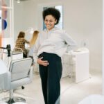 A smiling pregnant woman stands in a stylish nail salon, showcasing joy and relaxation.