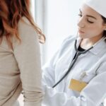 A female doctor in a white coat using a stethoscope during a patient examination.
