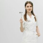 Female healthcare professional posing confidently in a white coat holding a reflex hammer.