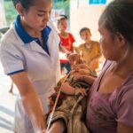 Healthcare worker assisting mother with infant in rural Laos clinic.