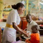 A nurse attends to a young patient while a guardian looks on in a hospital ward.