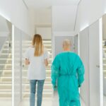 Two medical practitioners walking down a bright clinic hallway with reflections in mirrors.