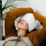 Woman in warm sweater resting with head bandage, showcasing cozy recovery indoors.