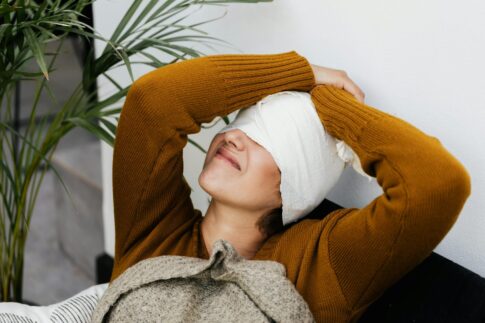 Woman in warm sweater resting with head bandage, showcasing cozy recovery indoors.