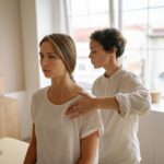 A woman receives shoulder therapy from a therapist in a serene room with natural light.
