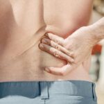 Close-up of a man holding his lower back in pain, possibly indicating discomfort or injury.