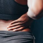 An adult of African descent holding their lower back in pain, indicating discomfort or injury.