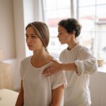A woman receives shoulder therapy from a therapist in a serene room with natural light.