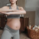 Fit pregnant woman doing yoga indoors, focusing on health and flexibility.