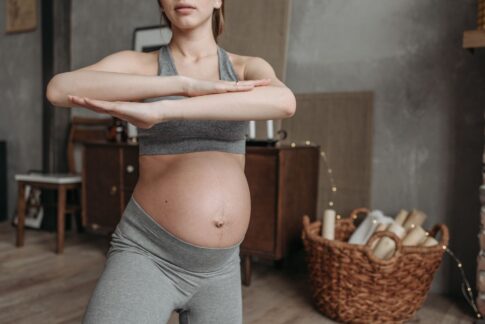 Fit pregnant woman doing yoga indoors, focusing on health and flexibility.