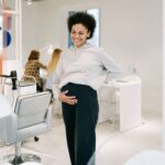 A smiling pregnant woman stands in a stylish nail salon, showcasing joy and relaxation.