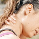Close-up of a woman holding her neck, showing discomfort and pain outdoors.