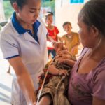 Healthcare worker assisting mother with infant in rural Laos clinic.