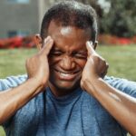 African American man massaging his temples outdoors, showing stress and emotion.