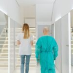 Two medical practitioners walking down a bright clinic hallway with reflections in mirrors.