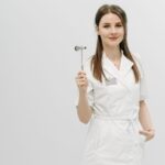 Female healthcare professional posing confidently in a white coat holding a reflex hammer.
