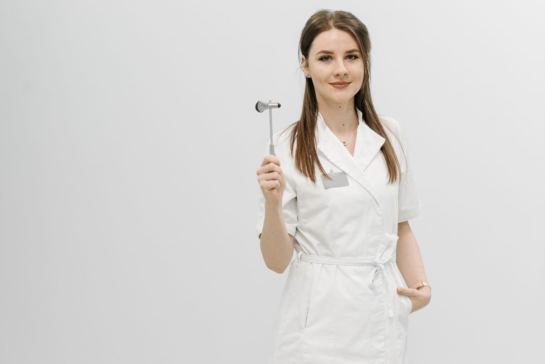 Female healthcare professional posing confidently in a white coat holding a reflex hammer.