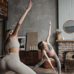 A pregnant woman practicing yoga with a trainer indoors, promoting a healthy lifestyle.