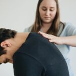 A physiotherapist assisting a patient with back pain in an indoor clinic setting.