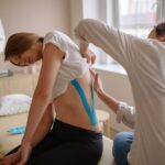 Chiropractor uses kinesio tape for pain relief on woman's back in a therapy session.