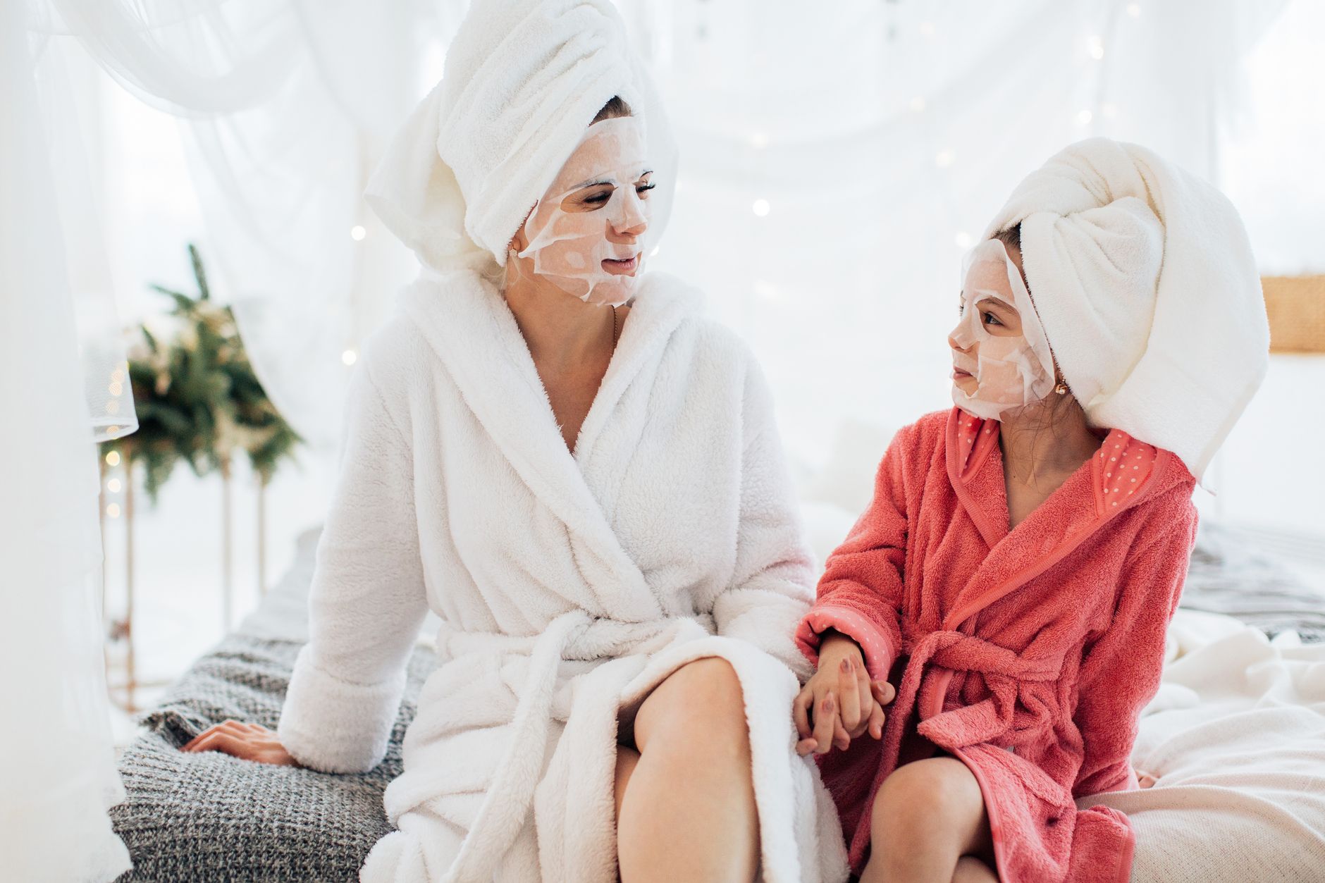 Mother and daughter bonding with face masks and robes, enjoying a spa day at home.