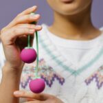 Detailed close-up of hands holding purple Kegel balls against a purple background.