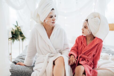 Mother and daughter bonding with face masks and robes, enjoying a spa day at home.