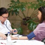 A healthcare worker measures a woman's blood pressure in an outdoor setting, emphasizing wellness and care.