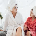Mother and daughter bonding with face masks and robes, enjoying a spa day at home.