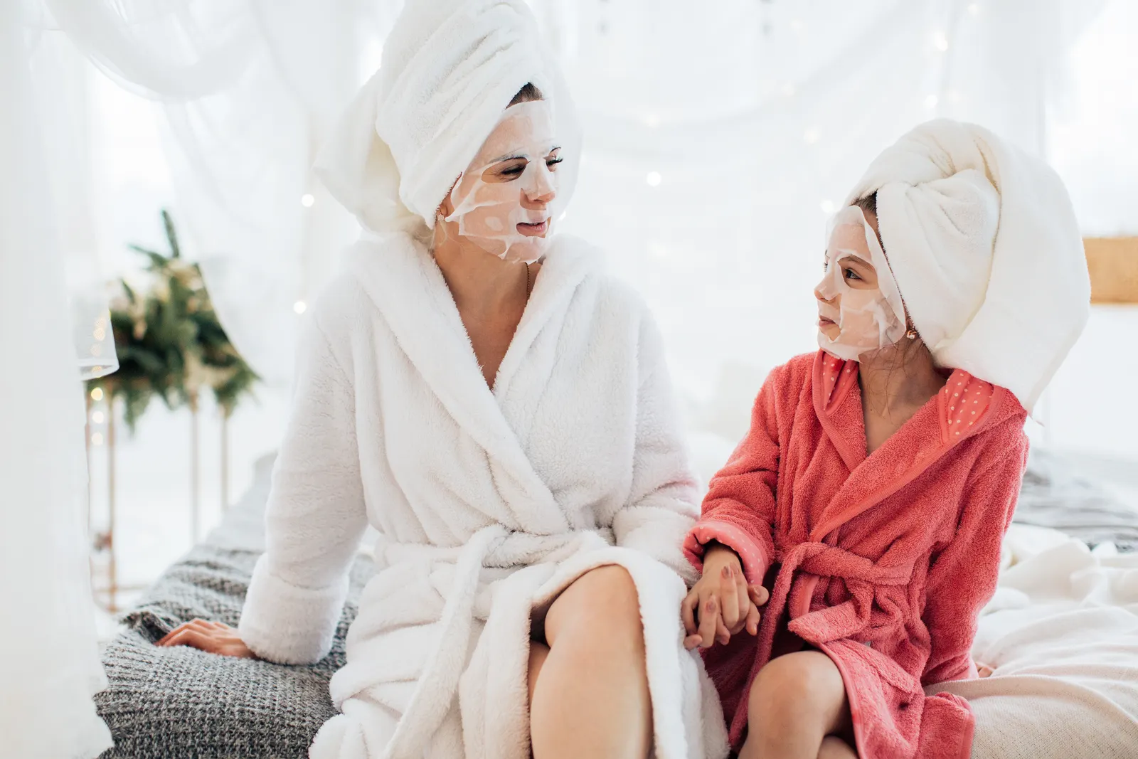 Mother and daughter bonding with face masks and robes, enjoying a spa day at home.