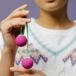 Detailed close-up of hands holding purple Kegel balls against a purple background.